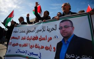 Palestinians take part in a demonstration demanding the release of Palestinian journalist Mohammed al-Qiq (portrait) from Israeli jails, next to the Jewish settlement of Beit El, north of Ramallah on January 22, 2016. Qiq, a 33-year-old reporter for Saudi TV channel Al Majd, was arrested on November 21 at his home in the West Bank city of Ramallah and in mid-December placed under administrative detention, which allows imprisonment without trial for six-month periods renewable indefinitely. / AFP / ABBAS MOMANI